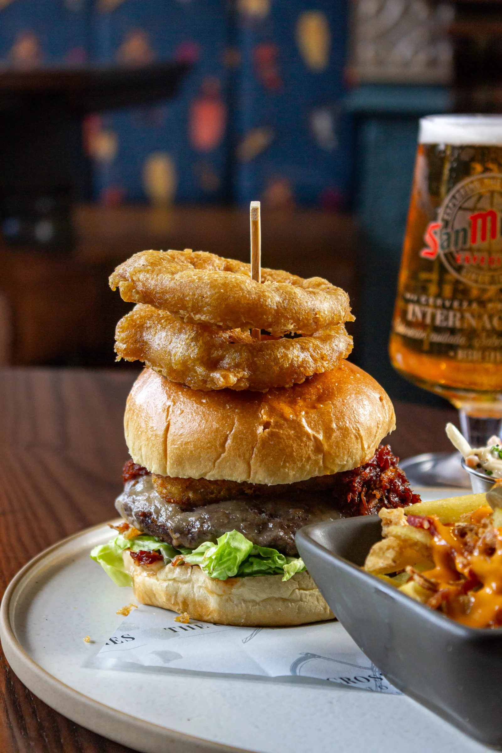 A burger stacked high with onion rings, a pint of beer and loaded fries at The Cross Scythes Totley
